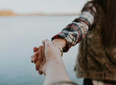 A couple holding hands in front of a lake.