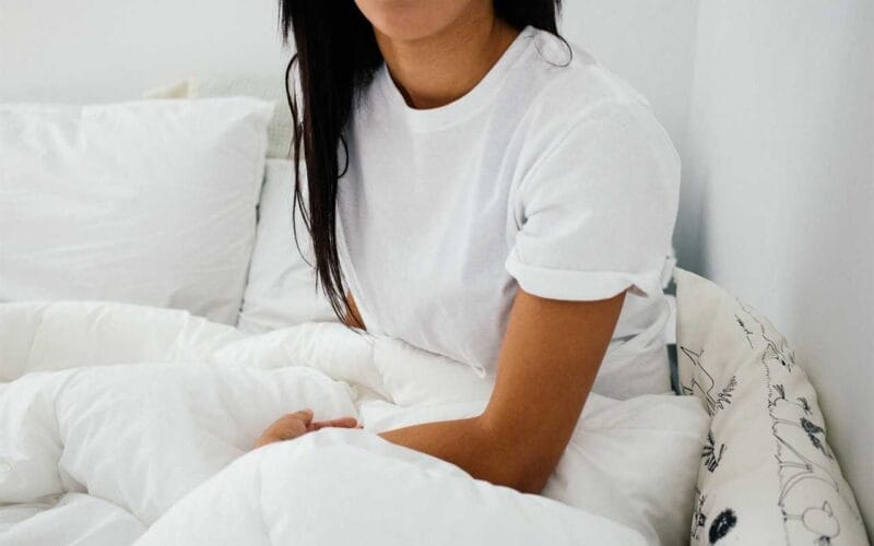 A woman in a white shirt sitting on a bed.