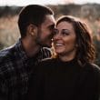 A couple is embracing in a field during their engagement session.