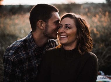 A couple is embracing in a field during their engagement session.