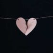 A broken heart hanging from a string on a black background.