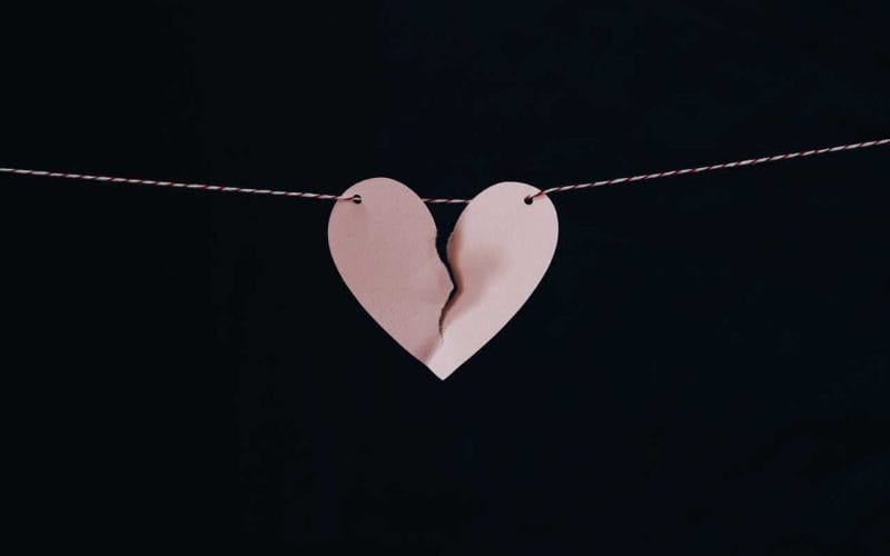 A broken heart hanging from a string on a black background.