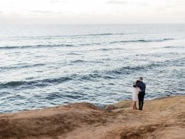 A couple standing on top of a cliff overlooking the ocean.