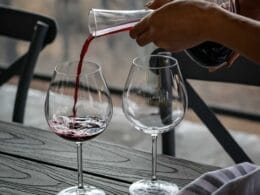 A person pouring wine into two glasses on a table.