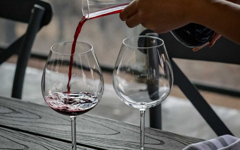 A person pouring wine into two glasses on a table.